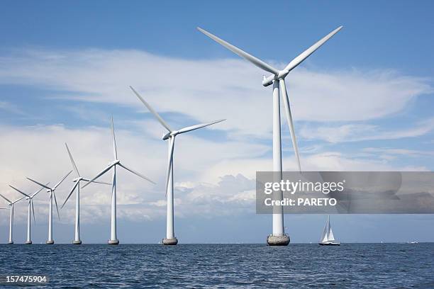 large white windmills in the sea with a sailboat - wind power stock pictures, royalty-free photos & images