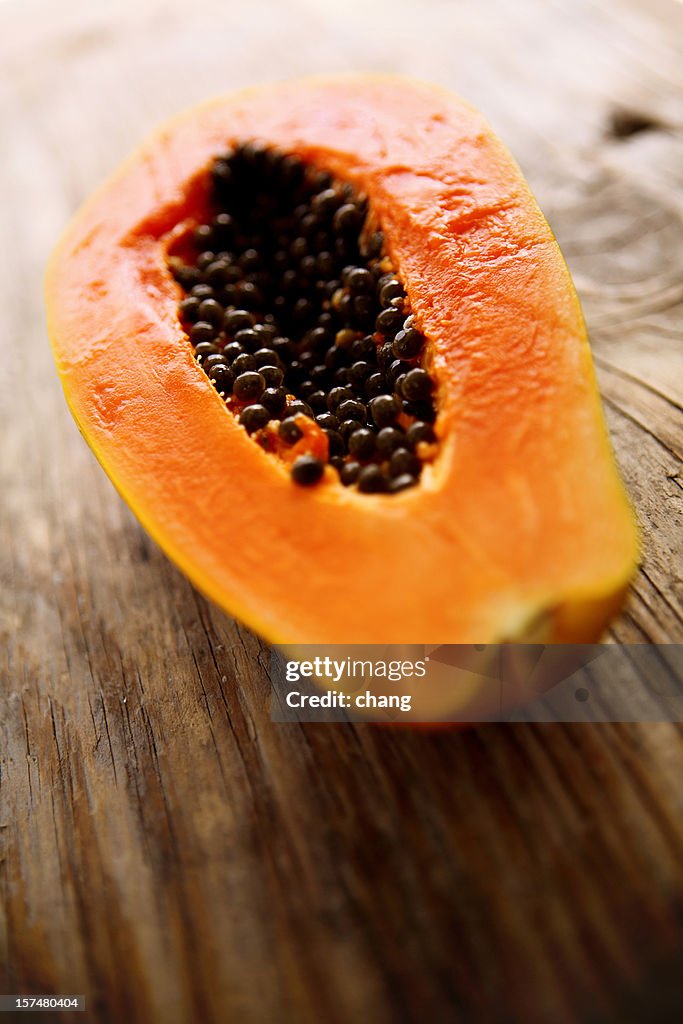 A halved fresh papaya on a wooden surface