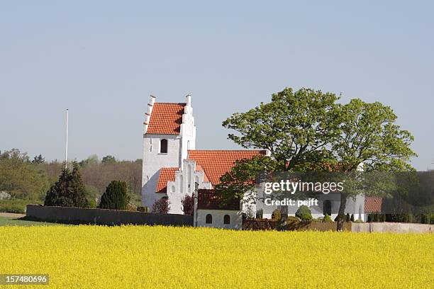 idyllic country side parish church behind oilseed rape field - pejft stock pictures, royalty-free photos & images