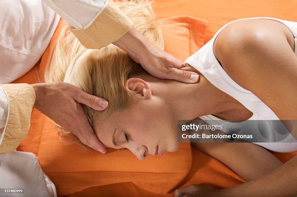 A woman is laying down while hands massage her head