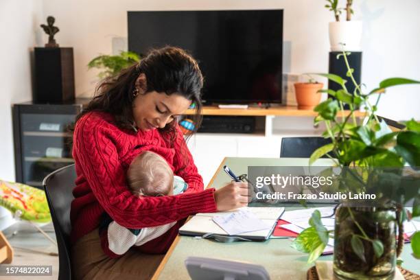 young mom working home office while hold her baby on lap at home - suckling stock pictures, royalty-free photos & images