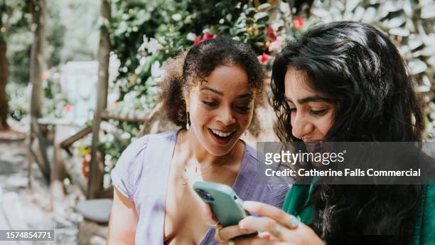 two young, beautiful woman, look at a mobile phone together - dating stockfoto's en -beelden