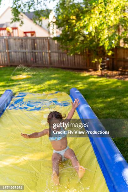 happy toddler girl playing on slip n' slide in backyard - hot american girl stock pictures, royalty-free photos & images