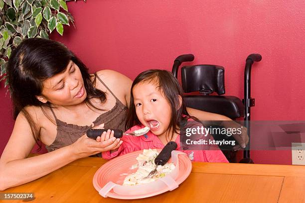 mother helps daughter use adaptive silverware - filipino family eating stock pictures, royalty-free photos & images
