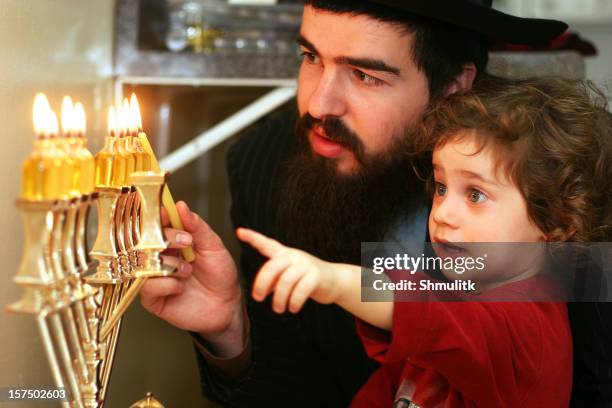 child watching father lighting the menorah - menorah lights stock pictures, royalty-free photos & images