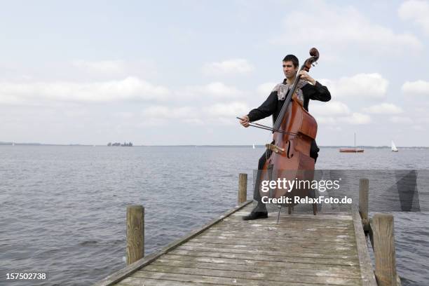 young male musician playing double bass on lakeside jetty (xxxl) - bass player stock pictures, royalty-free photos & images