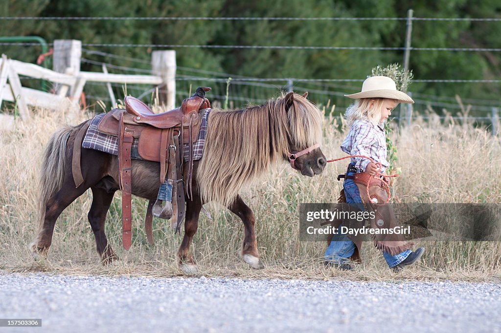 Small child in cowboy outfit with cute hairy pony on a lead