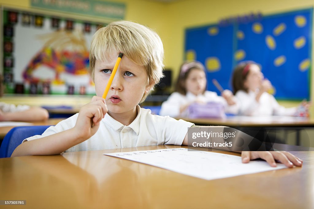 Escola primária: Jovem rapaz se concentre sobre um desafio maths problema