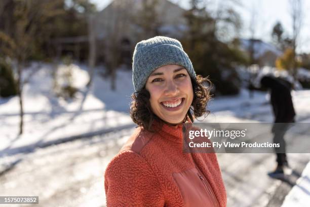 young eurasian woman smiles while playing in the snow with family - ski jacket stock pictures, royalty-free photos & images