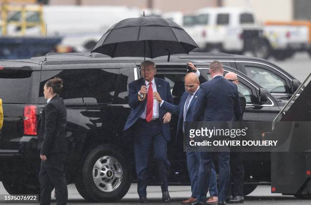 Walt Nauta, aide to former US President and 2024 hopeful Donald Trump, hands an umbrella to Trump while arriving to Ronald Reagan Washington National...