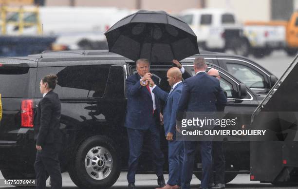 Walt Nauta, aide to former US President and 2024 hopeful Donald Trump, hands an umbrella to Trump while arriving to Ronald Reagan Washington National...