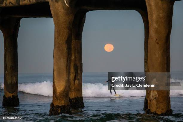 Manhattan Beach, CA A pre-dawn surfer is seen with the setting Hunter's full moon, behind the Manhattan Beach Pier, in Manhattan Beach, CA, Manhattan...