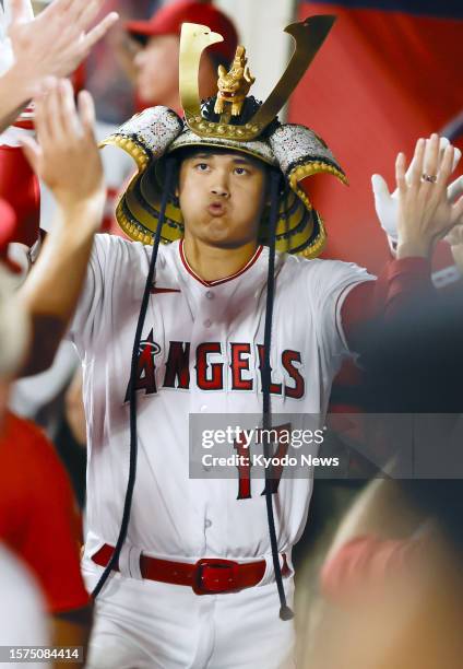 Los Angeles Angels two-way player Shohei Ohtani celebrates with teammates in the dugout while wearing a kabuto helmet after hitting a solo home run...