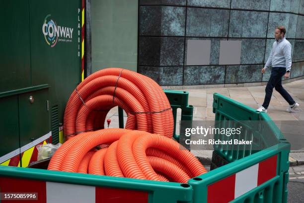 Man walks past barriers that contain plastic pipe collars, part of street works by contractor Conway, in the City of London, the capital's financial...