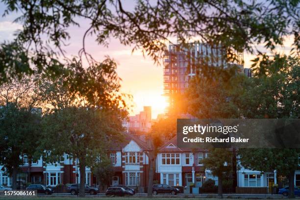 Orange glow from a setting summer sun which sinks below the skyline of new high-rise development at Higgs Yard and period Lambeth Edwardian homes in...