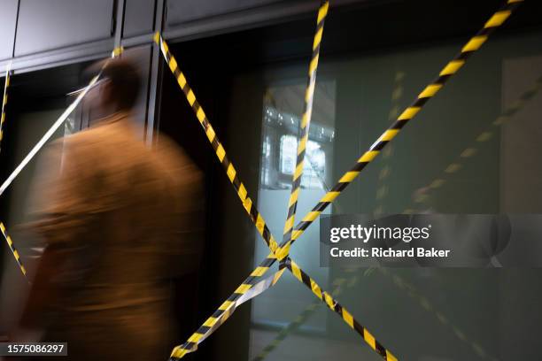 City worker walks past criss-crossed hazard tape in the City of London, the capital's financial district, on 3rd August 2023, in London, England.