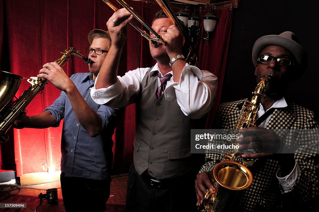 Three jazz musicians playing music with red curtain in back