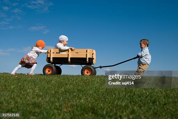 drei kinder schieben, ziehen und spielen mit wagon - ziehen stock-fotos und bilder