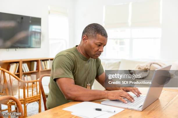 mature male soldier uses his computer to type an email to his family - veteran entrepreneur stock pictures, royalty-free photos & images