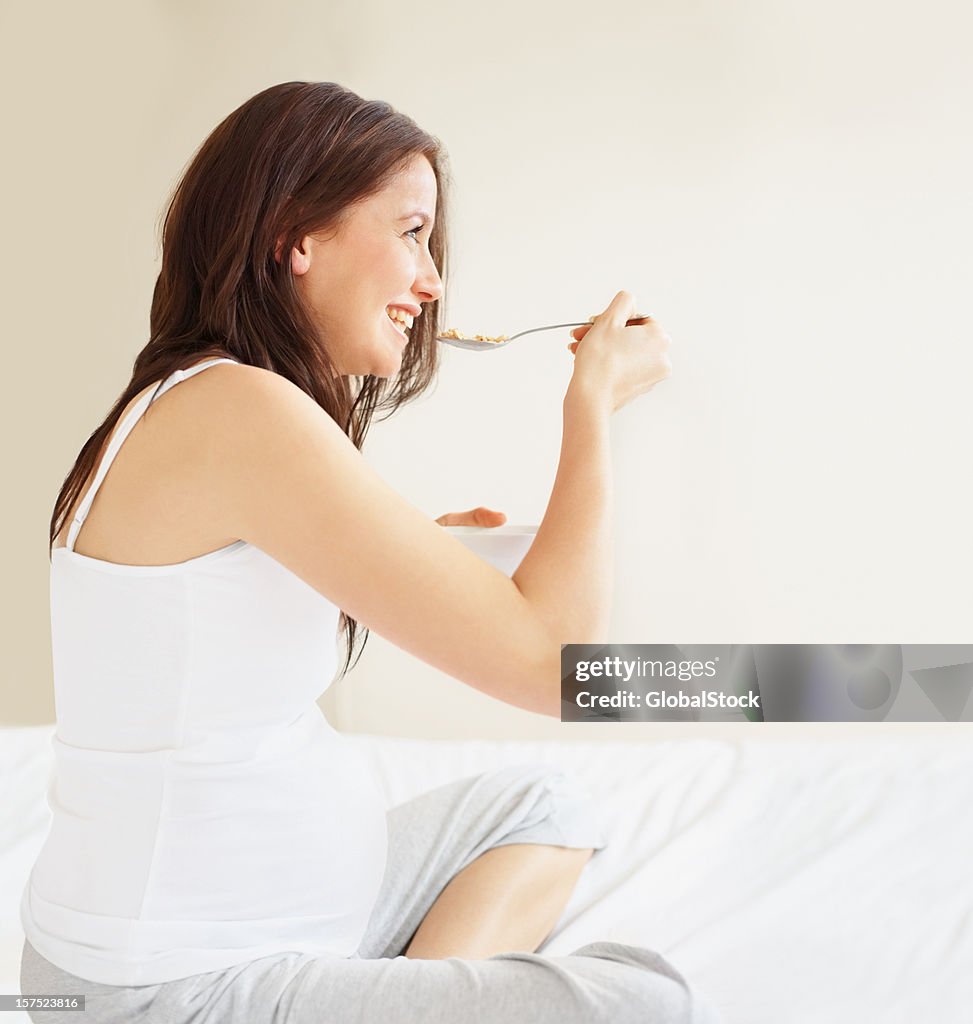 Giovane donna incinta avendo colazione a letto