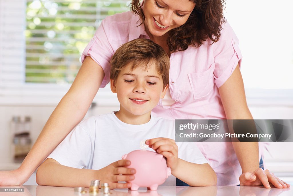 Menino com sua mãe colocando moedas no Mealheiro