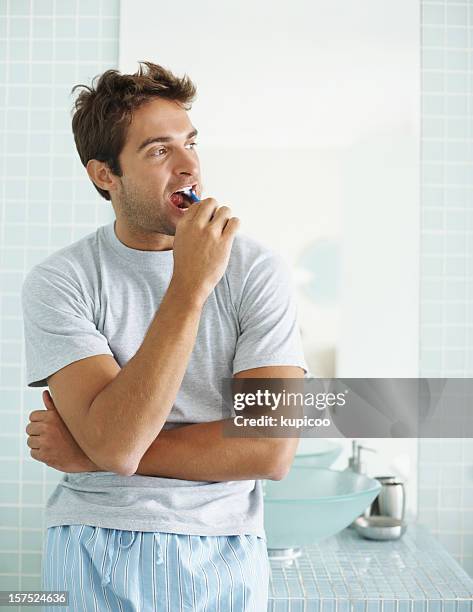 young guy brushing his teeth in  the bathroom - tandpasta stockfoto's en -beelden