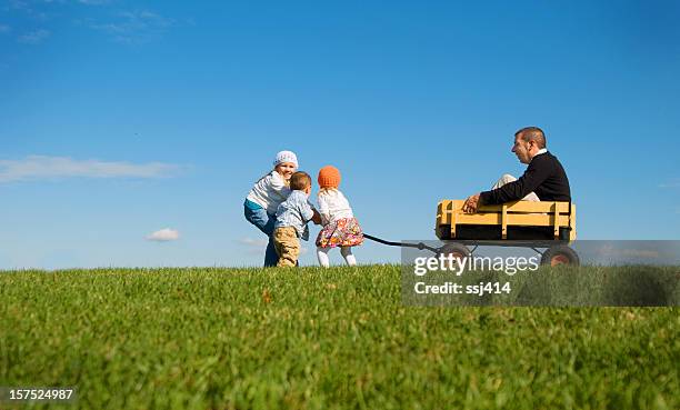 kinder ziehen daddy in wagon - bollerwagen mann stock-fotos und bilder