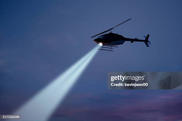 police helicopter shining a light beam in the dark sky - helikopter stockfoto's en -beelden