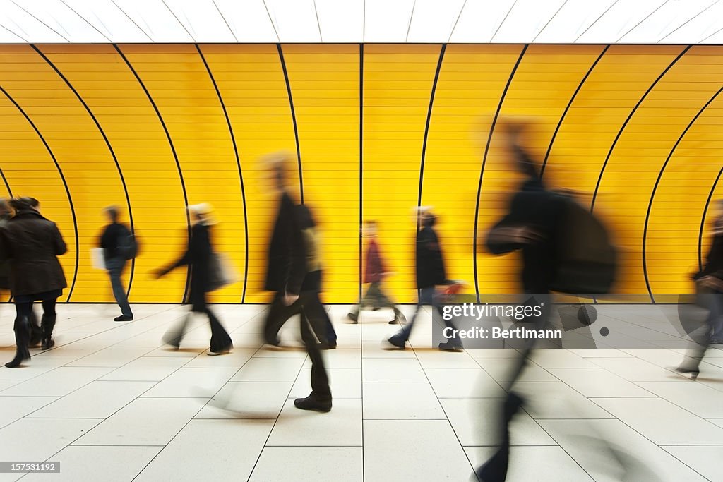 People blurry in motion in yellow tunnel down hallway