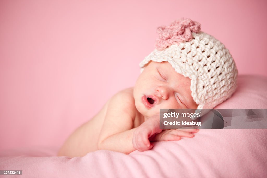 Sleeping Newborn Baby Girl Wearing a Crocheted Hat on Pink