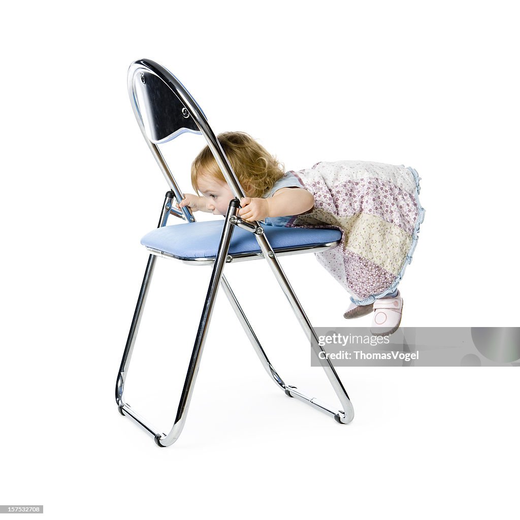 Cute 15 months girl climbing onto a blue chair