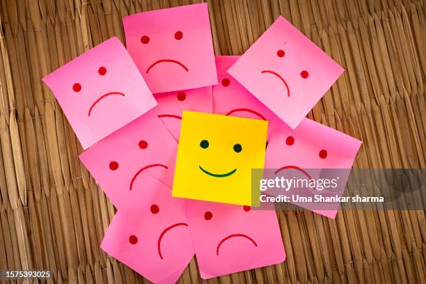 sad faces on sticky notes surrounding one happy one. - schadenfreude stock-fotos und bilder