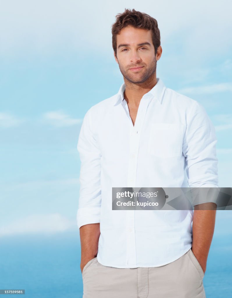 Young man with hands in pockets standing against blue sky