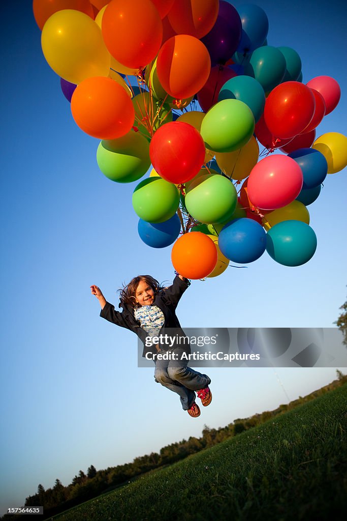 Happy Young Girl Jumping with a Bunch of Balloons Outside