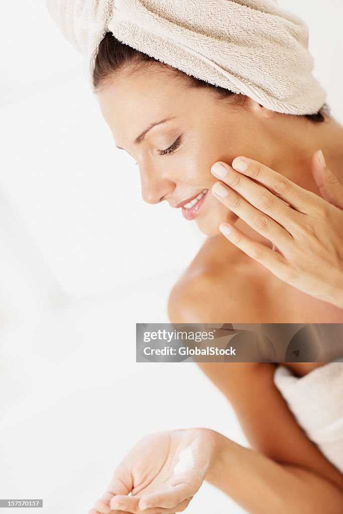 Woman applying face cream in towel after shower