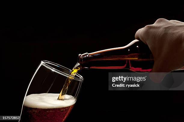 hand holding bier flasche gießen in ein glas isoliert auf schwarz - beer pour stock-fotos und bilder