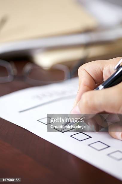 female hand holding pen about to make a check mark on paper - checklist stockfoto's en -beelden