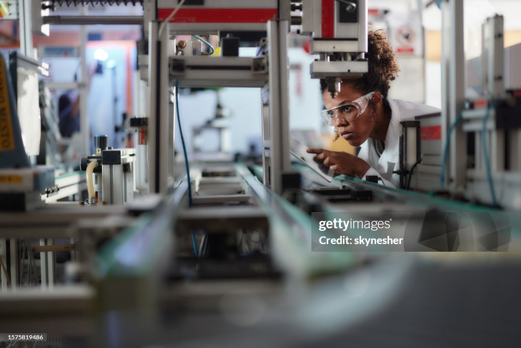 Young black scientist using touchpad while working on machinery in a lab.