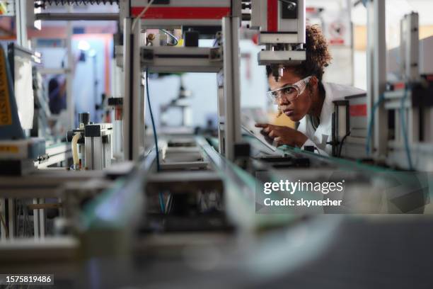 young black scientist using touchpad while working on machinery in a lab. - robotics stockfoto's en -beelden