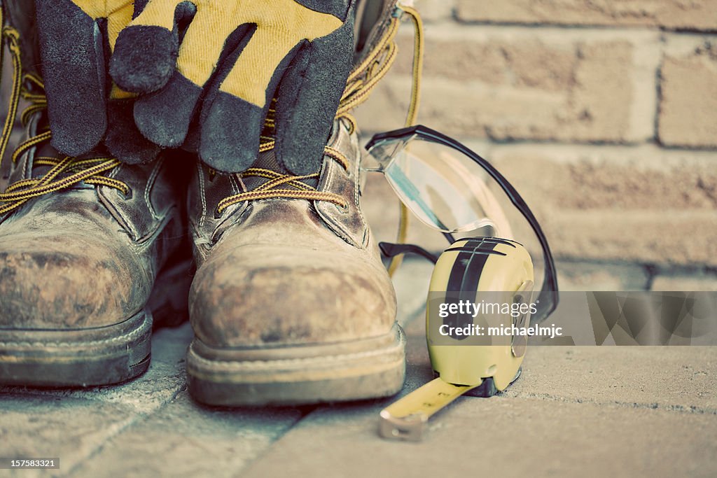Muddy construction work boots with gloves and tape measure