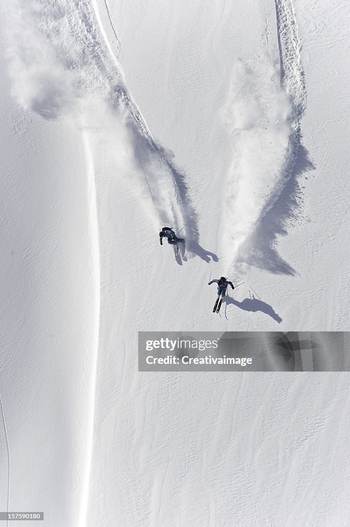 Aerial view of two skiers skiing downhill in powder snow