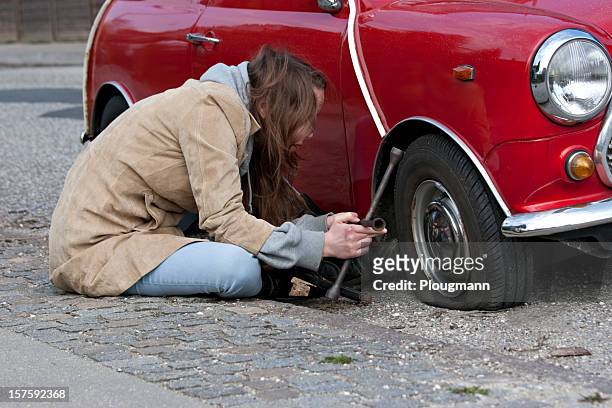 mujer joven cambios en su automóvil de neumáticos - flat tire fotografías e imágenes de stock