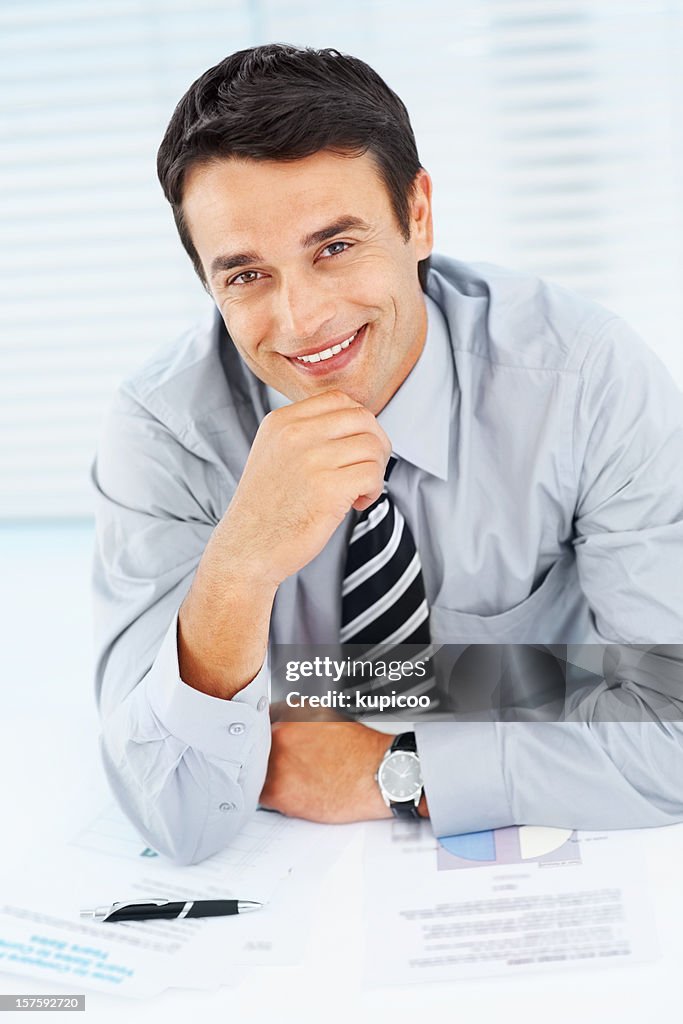Smiling executive sitting with hand on chin at desk