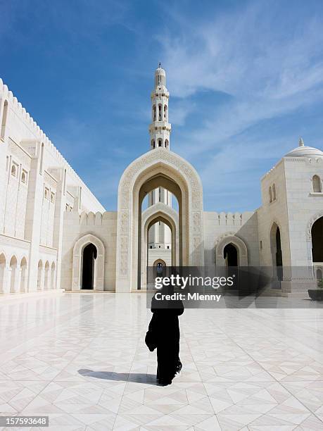 woman in abaya cloak walking towards archway of grand mosque - masqat oman stockfoto's en -beelden