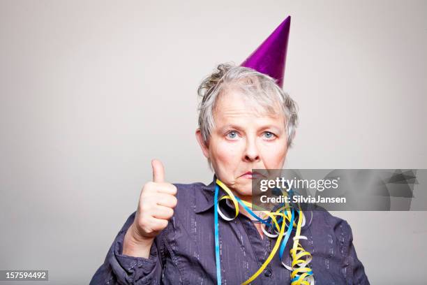 depressed senior woman doing thumbs up - party hat stock pictures, royalty-free photos & images