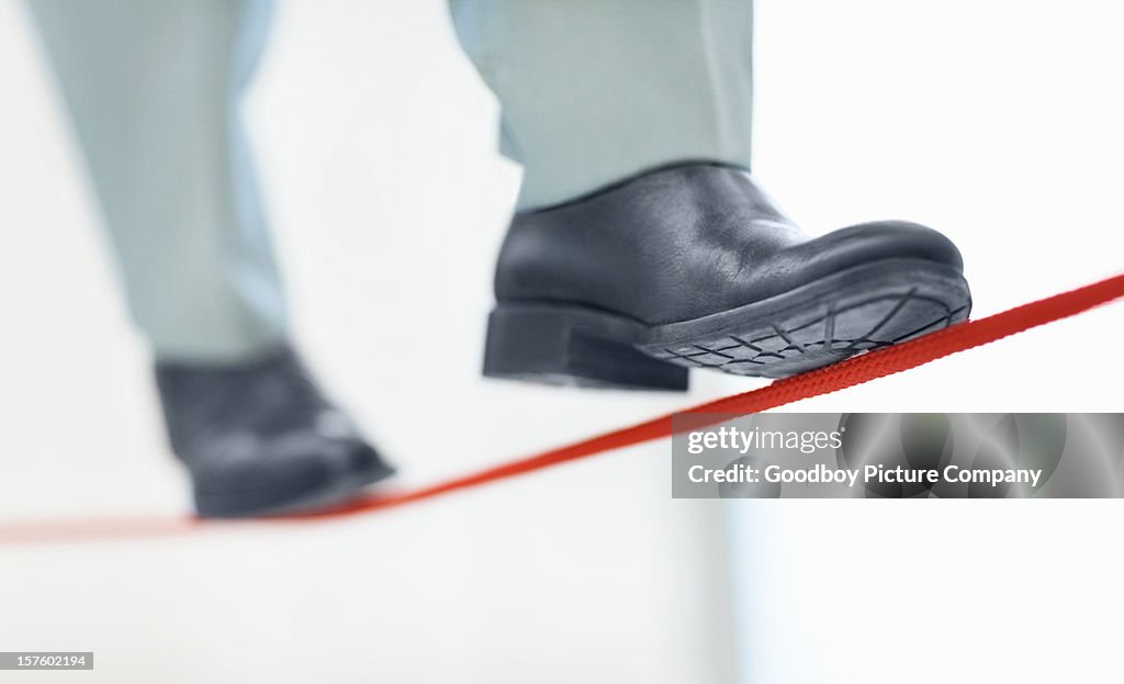 Business man walking on thin line depicting uncertainty job