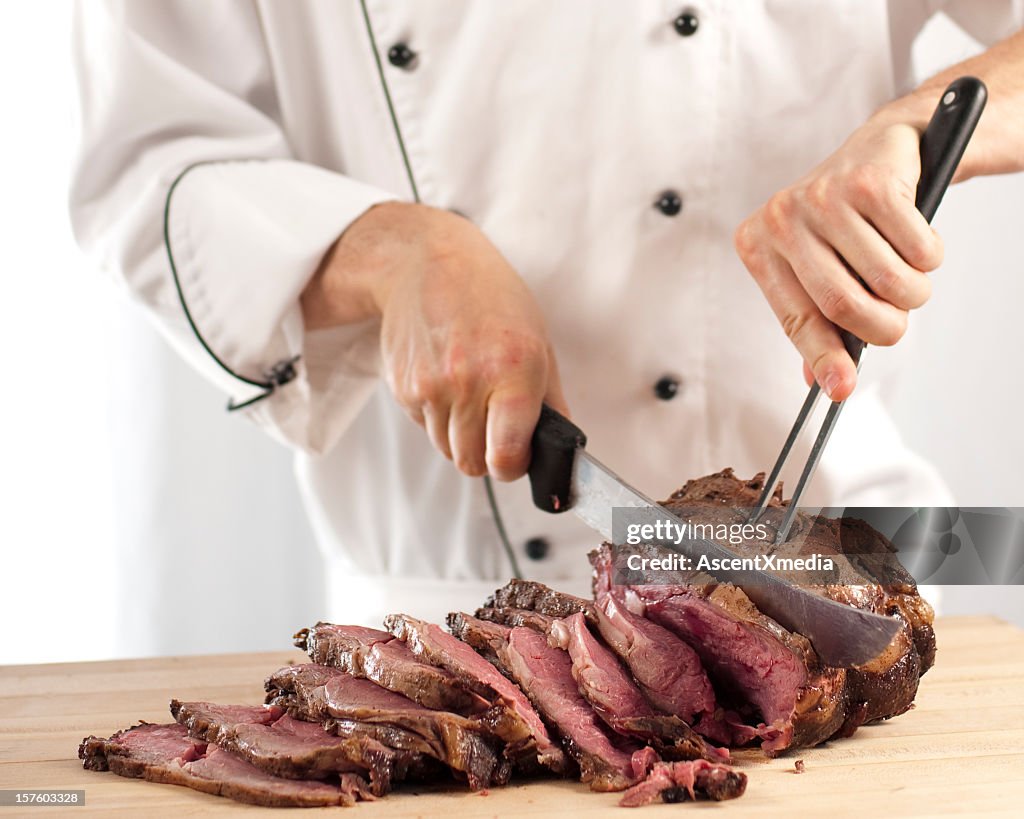 Chef slicing roast beef using carving knife and fork