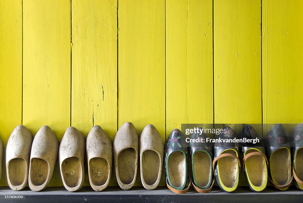 Fila di scarpe di legno contro un muro giallo