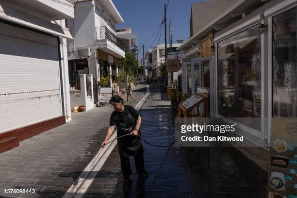 Staff member washes an area outside a restaurant ahead of opening on July 28, 2023 in Gennadi, Greece. The water had been turned back on after a...
