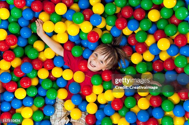smiling child playing in a colorful ball pit - multi coloured balls stock pictures, royalty-free photos & images